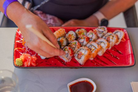 A close-up view of female hands using chopsticks to pick up sushi from a plate in a restaurant. Curacao.