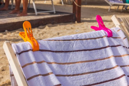 Close up view of sandy beach with sun loungers topped with beach towels and secured by clips. Curacao.