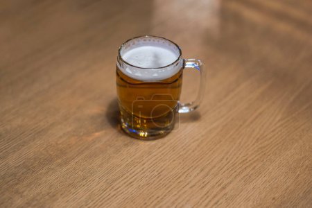 Close-up view of a beer mug filled with beer standing alone on a wooden table.