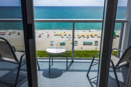 A beautiful view from the upper floor of the hotel room, through the open balcony door, overlooking the sandy beach of Miami Beach. 