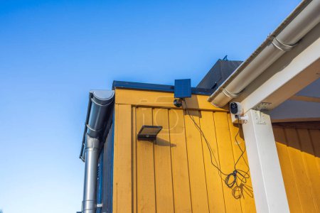 Nahaufnahme einer Outdoor-Überwachungskamera und einer Outdoor-Lampe mit Solarzellen an der Fassade einer Villa an einem sonnigen Tag. Schweden.