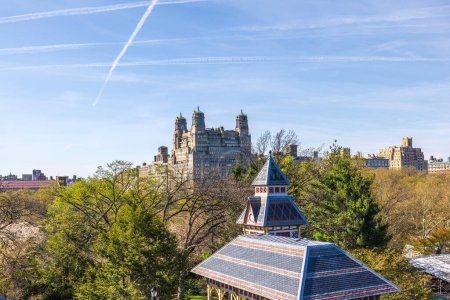 Beautiful view of Belvedere Castle in Central Park, New York City, with contrasting modern skyscrapers in the background and striking jet trails in the blue sky. USA.