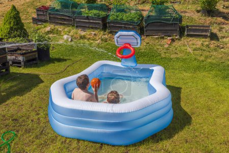 Photo for Two boys in an outdoor inflatable pool playing a game of water basketball in the backyard on a sunny summer day. Sweden. - Royalty Free Image