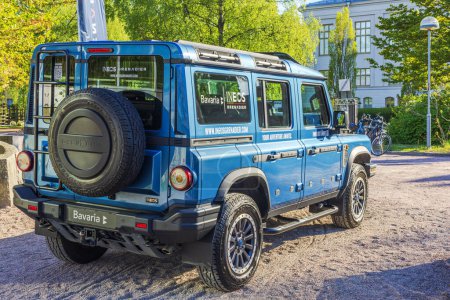 Foto de Close-up view of a blue INEOS Grenadier off-road vehicle parked outdoors, showcasing its rugged design and branding in a sunny urban setting. - Imagen libre de derechos