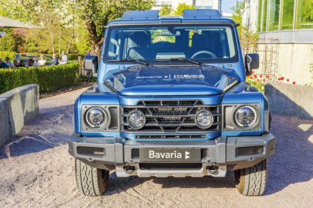 Foto de Close-up view of the front of a blue INEOS Grenadier off-road vehicle, highlighting its robust grille and headlights, displayed in a sunny outdoor setting. - Imagen libre de derechos