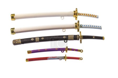 Close-up view of a collection of miniature toy swords in colorful scabbards, including katana and wakizashi isolated on white background.