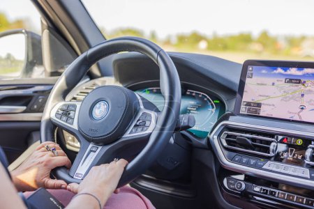 Téléchargez les photos : Vue rapprochée des mains féminines sur le volant d'une voiture électrique BMW iX3 M circulant sur l'autoroute un jour d'été. - en image libre de droit