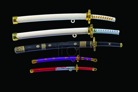 Close-up view of a collection of miniature toy swords in scabbards, including katana and wakizashi isolated on black background.