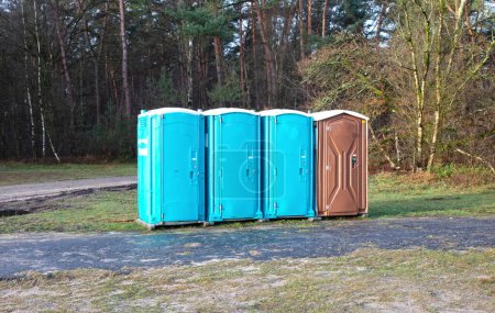Téléchargez les photos : Quatre toilettes mobiles sur une rangée dans la forêt néerlandaise - en image libre de droit
