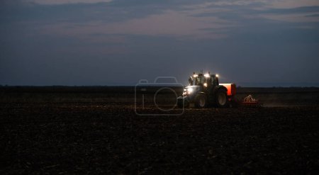 Tracteur préparant la terre avec cultivateur de lit de semence la nuit
.