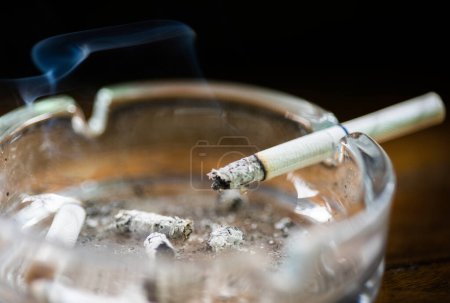 Glass ashtray with lit cigarette on a wooden table