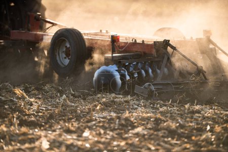 Un agriculteur dans un tracteur prépare son champ alors que le soleil commence à se coucher. 