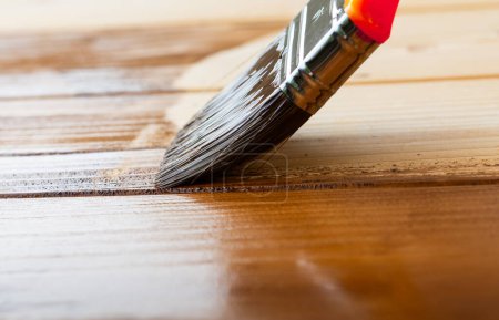 Cepillo que cubre tablones de madera y vigas con barniz para trabajos interiores 