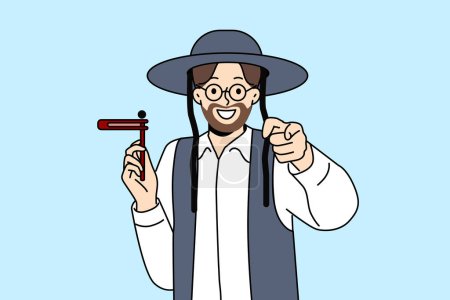 Illustration for Orthodox jewish man with wooden grager ratchet in hand points finger at screen congratulating you on holiday of hanukkah. Israeli resident preaches judaism invites to celebrate hanukkah with smile - Royalty Free Image