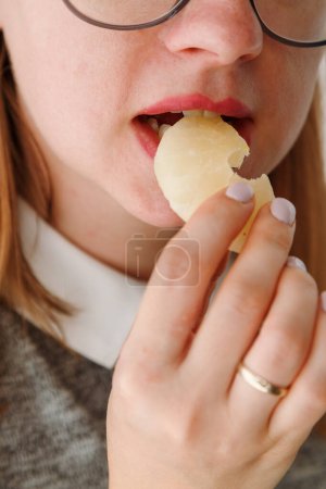 Gros plan d'une bouche de femme mangeant de l'ananas séché, une collation saine pour les élèves. Amateurs de nourriture sucrée, comment manger sucrée et rester en bonne santé.