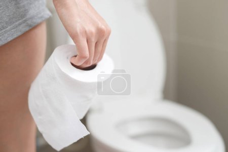 Téléchargez les photos : Portrait d'une femme souffre de diarrhée son estomac douloureux. mal et problème. tenir à la main rouleau de papier de soie devant le bol de toilette. constipation dans la salle de bain. Hygiène, concept de santé. - en image libre de droit