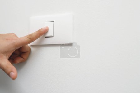 Téléchargez les photos : Éteignez la lumière, fermez le doigt main de l'homme ferme le commutateur d'alimentation avec mur à la maison pour économiser de l'énergie. réduire le réchauffement climatique. - en image libre de droit