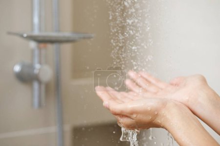 Foto de Una mujer utiliza la mano para medir la temperatura del agua de un calentador de agua antes de tomar una ducha - Imagen libre de derechos