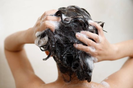 Foto de Mujer tomando ducha y lavando el cabello con champú en el baño en casa - Imagen libre de derechos