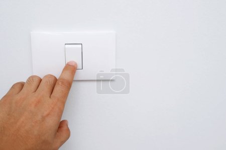 Éteignez la lumière, fermez le doigt main de l'homme ferme le commutateur d'alimentation avec mur à la maison pour économiser de l'énergie. réduire le réchauffement climatique.