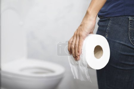 Photo for Portrait of a woman suffers from diarrhea his stomach painful. ache and problem. hand hold tissue paper roll in front of toilet bowl. constipation in bathroom. Hygiene, health care concept. - Royalty Free Image