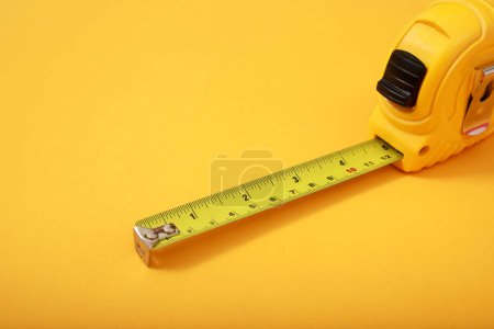 Téléchargez les photos : Le ruban à mesurer jaune pour le maçon est placé sur un fond jaune. Concentration douce. - en image libre de droit