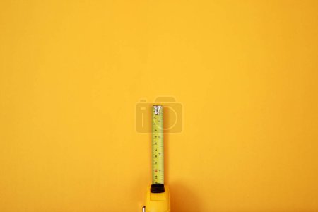 Téléchargez les photos : Le ruban à mesurer jaune pour le maçon est placé sur un fond jaune. Concentration douce. - en image libre de droit