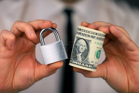 Foto de Empresario sosteniendo un candado de plata y un paquete de dólares en su mano. Seguridad monetaria. - Imagen libre de derechos