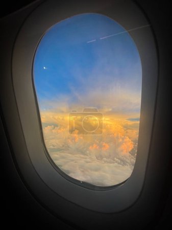 Téléchargez les photos : Regarder par la fenêtre de l'avion dans le coucher du soleil dans les nuages - en image libre de droit