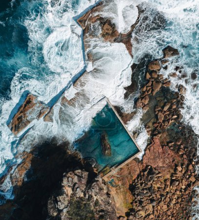 Aerial view early morning light with ocean waves flowing over rocks around North Curl Curl ocean rock pool during storm. Photo taken in Australia.
