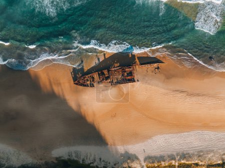 Foto de Kgari Alto ángulo de las aves aéreas vista del dron del ojo del naufragio Maheno en Seventy-Five Mile Beach en Fraser Island, Queensland, Australia. Hermosa luz del atardecer con olas - Imagen libre de derechos