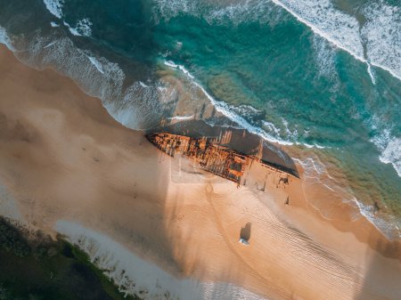 Foto de Kgari Alto ángulo de las aves aéreas vista del dron del ojo del naufragio Maheno en Seventy-Five Mile Beach en Fraser Island, Queensland, Australia. Hermosa luz del atardecer con olas - Imagen libre de derechos