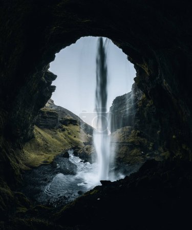 Téléchargez les photos : Cascade de Kvernufoss dans les gorges des montagnes. Attraction touristique Islande. Homme en veste rouge debout et regarde le flux de l'eau qui tombe. Beauté dans la nature
. - en image libre de droit