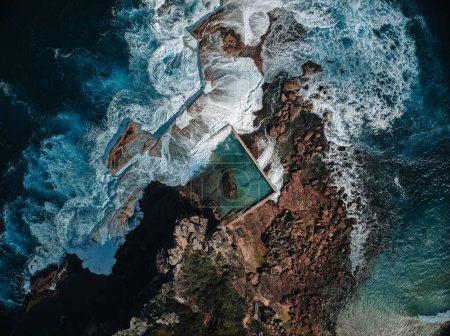 Vista aérea a primera hora de la mañana con olas oceánicas que fluyen sobre rocas alrededor de la piscina de rocas North Curl Curl Ocean durante la tormenta. Foto tomada en Australia.