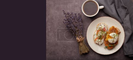 Foto de Desayuno estético - sándwiches con huevo escalfado, salmón, alfalfa, semillas de chía, guisantes germinados, taza de café cerca de flores de lavanda. Banner extra ancho. - Imagen libre de derechos
