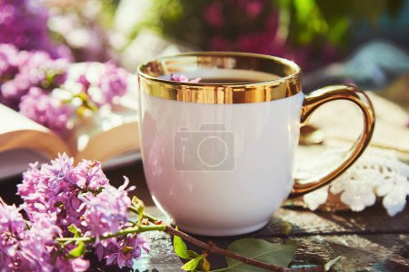 Téléchargez les photos : Pause café avec une tasse de café parmi les fleurs lilas. Lire un livre, concept de détente et de loisirs. Esthétique chalet style de vie de base. - en image libre de droit
