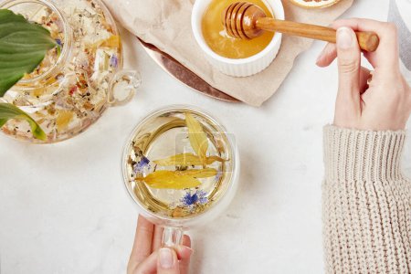 Las manos de mujer añaden miel a la taza de té. Estilo de vida saludable té de hierbas de montaña. Concepto de hierbas desintoxicantes