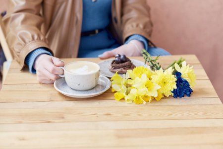 Téléchargez les photos : Pause café confortable - femme savourant latte et dessert au chocolat avec jonquilles de printemps. - en image libre de droit