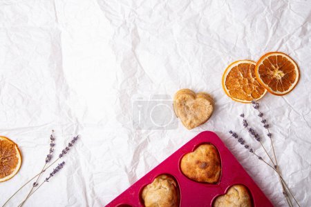 Téléchargez les photos : Gâteaux faits maison en forme de cœur sur un moule rose vif, avec agrumes secs et accents de lavande. - en image libre de droit