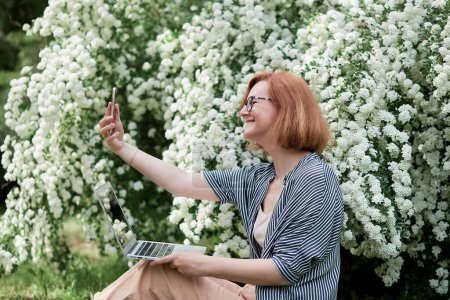 Photo for Freelance lifestyle, remote work in full bloom a young woman captures her moment among white flowers with laptop. - Royalty Free Image