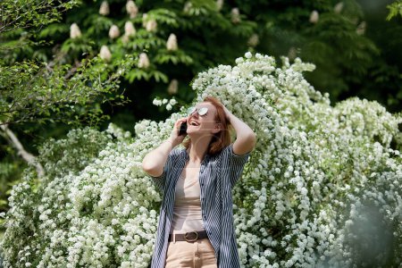 Photo for Freelance lifestyle - red-haired woman takes a call surrounded by spring flowers. - Royalty Free Image