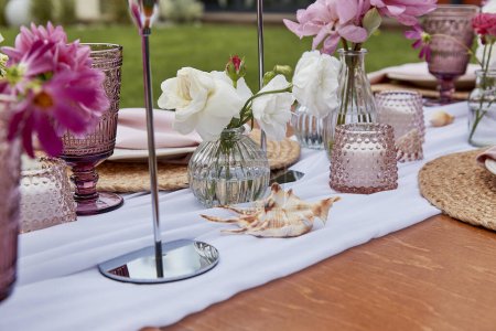 Téléchargez les photos : Cadre de table esthétique pique-nique rose, arrangement de fleurs, coquillages rapprochés. Configuration confortable avec des fleurs et des bougies. - en image libre de droit