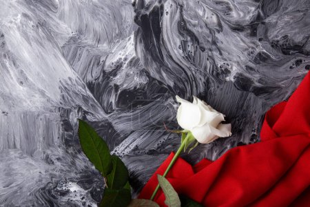 White rose on abstract monochrome texture with vibrant red fabric. Copy space.