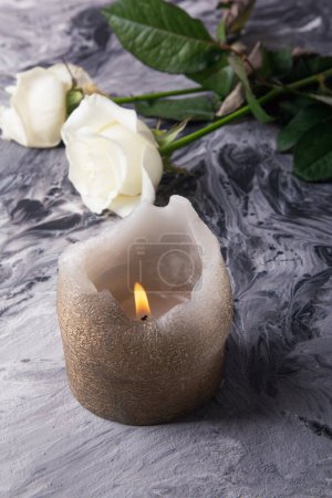 Tranquil candle and white roses on an abstract gray textured background.