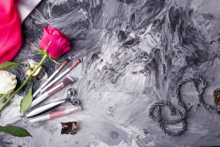Glamorous makeup tools and fresh flowers set against a monochrome fluid art background.