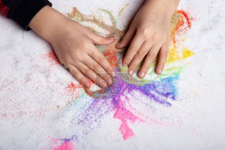 Kinderhände spielen mit regenbogenfarbenem Sand. Motorik, kindliche Kreativität.