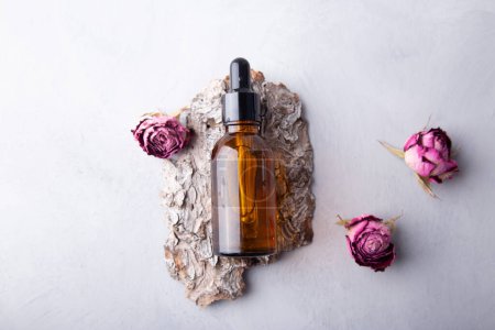 Essential oil bottle with dried roses on bark minimalist natural skincare presentation.