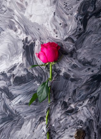 Eine einzelne rosa Rose auf monochromer flüssiger Kunst. Zarte florale Schönheit trifft auf dramatische abstrakte Texturen.