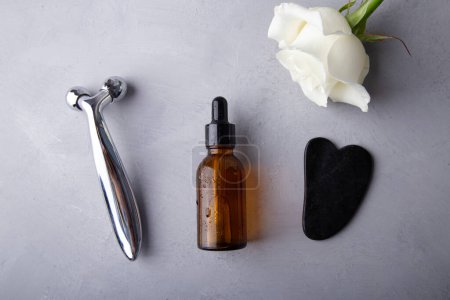 Luxurious skincare routine with a white rose and facial tools on a grey backdrop.