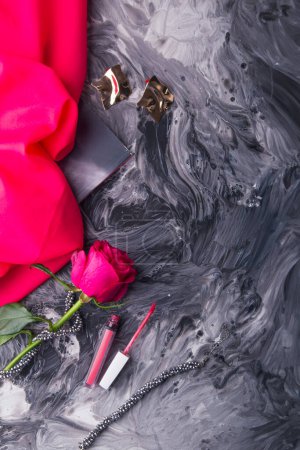 Glamorous makeup tools and fresh rose set on monochrome fluid art background.